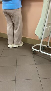 Clinic reception desk, rear view, woman standing at the counter in casual clothes, light trousers, light blue sweater, sneakers, tiled floor