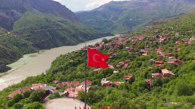 Drone shot revealing Kemaliye village through a waving Turkish flag. Aerial view of the historic town and Karasu River canyon nestled in the mountains of Erzincan, Turkey