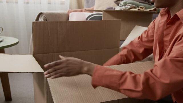 Tilt up midsection view of African American girl packing clothing items for donation and sealing box with packaging tape