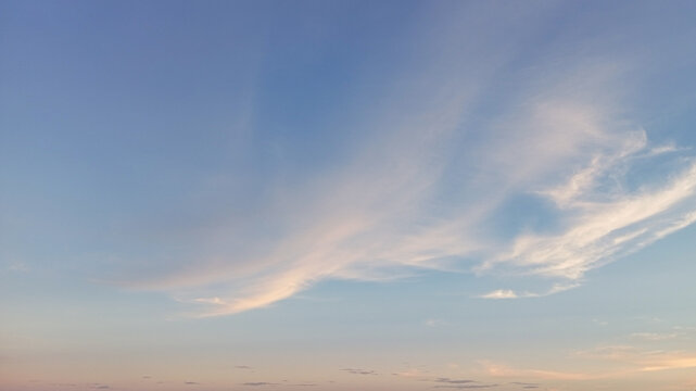 Scenic low angle view of vibrant blue sky covered with wispy white cirrus clouds. Soft warm gradient colors near the horizon during sunset or sunrise, perfect for inspirational backdrops
