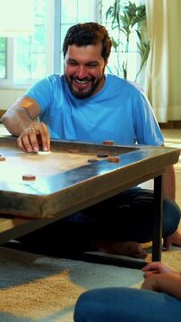 Family playing carrom board game together at home, enjoying bonding time with young children