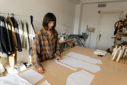 Fashion designer arranging paper pattern pieces on table in small sewing studio atelier