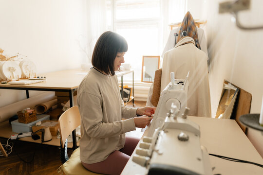 Woman sewing at a domestic studio sewing machine in a bright home atelier workspace