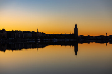 Naklejka premium Stockholm, Sweden The sun rises above Kungsholmen and the City Hall, Stadshuset, in the Riddarfjarden Bay in downtown.