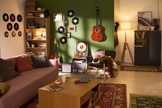 Wide angle shot of music themed living room featuring guitar, vinyl records, sofa, shelving, and coffee table. Supporting home decor, rental listing, interior design, lifestyle marketing