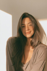 Fototapeta premium young thai woman taking selfie indoors in natural light, casual asian female portrait with smartphone and soft lighting, authentic no makeup selfie of young thai woman with long dark hair