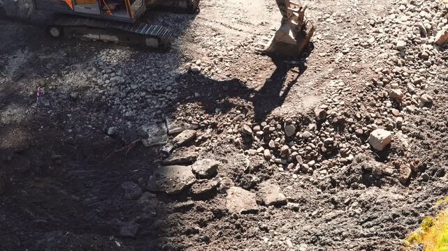 High angle view of a yellow excavator clearing rocky and muddy ground at a site