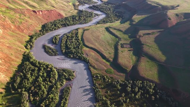 Aerial flight over Naryn River meanders through eroded red landscape at sunset near Eki-Naryn, Kyrgyzstan