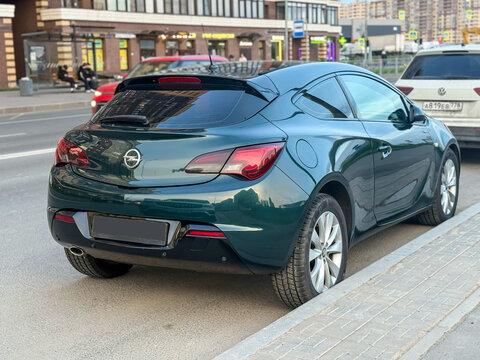 Green Opel Astra J GTC in the city street. Motor sports car Opel Astra J GTC hot hatch in the city street. Opel Astra GTC OPC hatchback. German sport hatchback. Opel Z18XER 1.8 Ecotec petrol engine. 