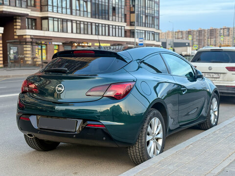 Green Opel Astra J GTC in the city street. Motor sports car Opel Astra J GTC hot hatch in the city street. Opel Astra GTC OPC hatchback. German sport hatchback. Opel Z18XER 1.8 Ecotec petrol engine. 