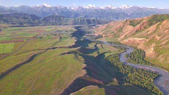 Wide drone panorama of Eki-Naryn village with cultivated fields along Naryn River and Tian Shan peaks, Kyrgyzstan
