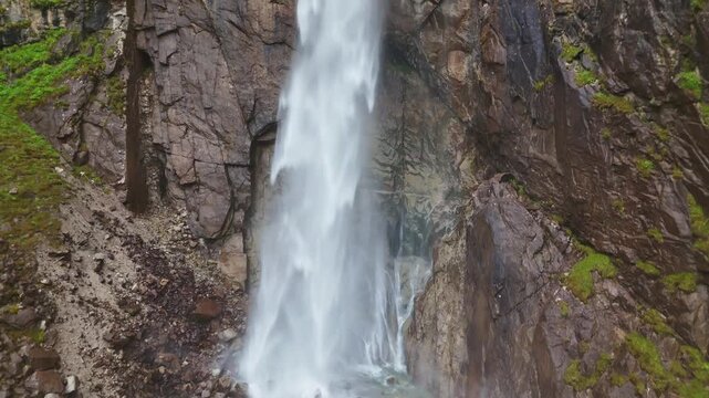 Close aerial of Barskoon Waterfall plunging over rock face surrounded by conifer trees, Kyrgyzstan