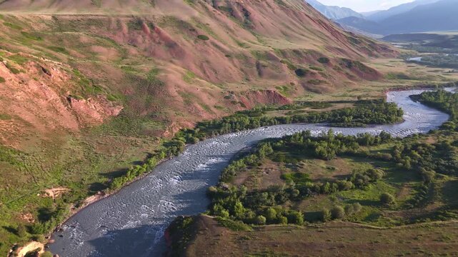 Aerial drone over Naryn River near Eki-Naryn with meandering water and red clay hillsides, Kyrgyzstan