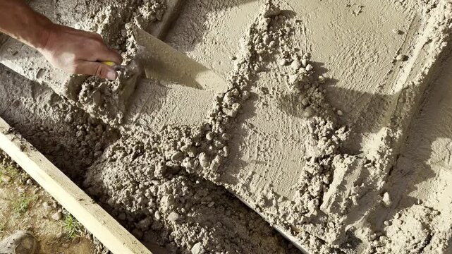 Hand using trowel to spread wet cement surface closeup