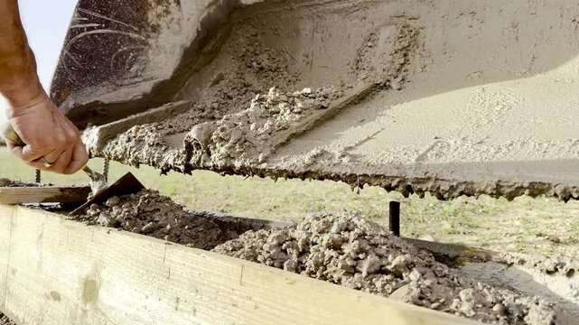 Hand using trowel to spread wet cement on foundation