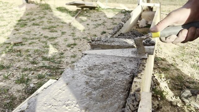 Worker hand using trowel to spread wet cement outdoors