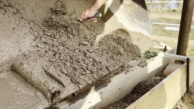 Hand using trowel to spread wet cement on wall base