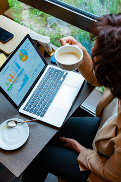 Business woman reviewing sales charts on laptop at cafe