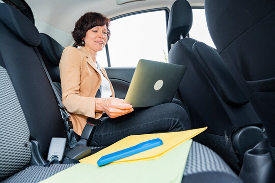 Business woman using laptop in car back seat on commute