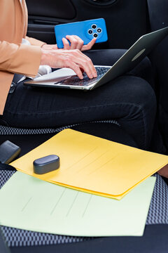 Businesswoman using laptop and phone while riding in car