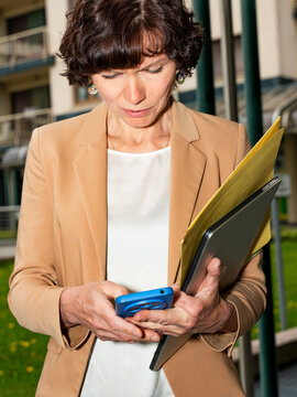 Business woman using smartphone while holding laptop and folder