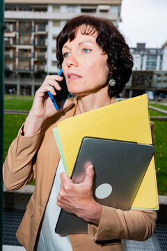 Businesswoman on phone with laptop and folders in city