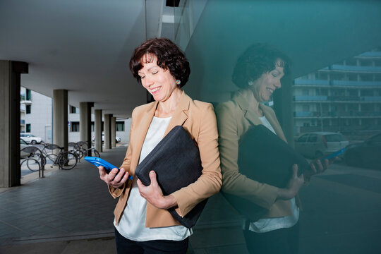 Businesswoman checking smartphone outside modern office building