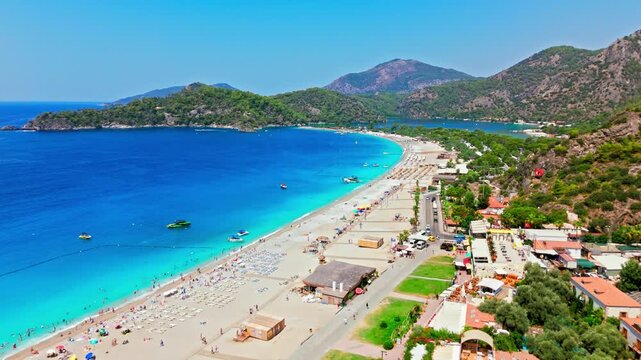 Drone view of Oludeniz Beach, Turkey coastline. Sandy shore, blue sea, beach umbrellas and green mountains create a sunny travel scene.