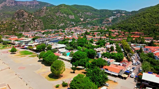 Oludeniz resort village on the southwest coast of Turkey. Red-roofed hotels, green mountains and sandy beach area create a sunny Mediterranean travel scene.