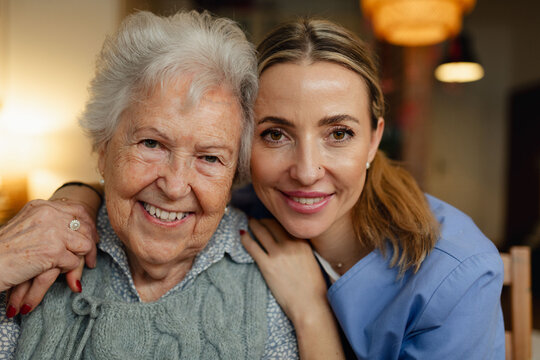 Portrait of caring healthcare worker visiting a senior patient at home, hugging her.