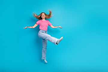 Fototapeta premium Joyful young woman in striped tshirt jeans jumps against blue background for lifestyle advertising and fashion promo