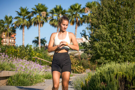 Focused runner checking smartwatch in sunny park
