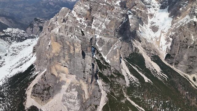 Aerial tracking along Civetta limestone wall with snow couloirs and vertical faces, Dolomites