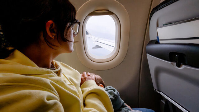 Passenger holding baby beside airplane window in flight