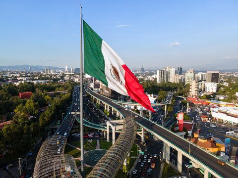 Toma a&eacute;rea de la bandera de M&eacute;xico en primer plano y en segundo las avenidas y edificios de la ciudad