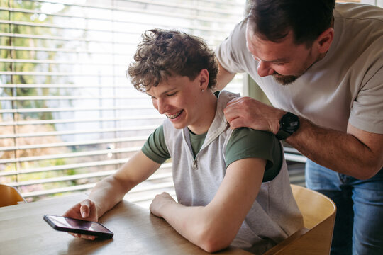Father supporting teenage son at home during everyday moment.