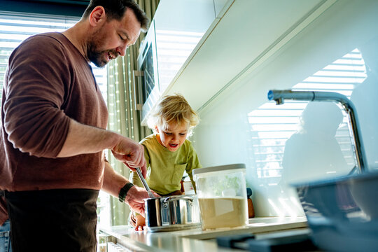 Dad and toddler preparing simple meal together in bright kitchen.