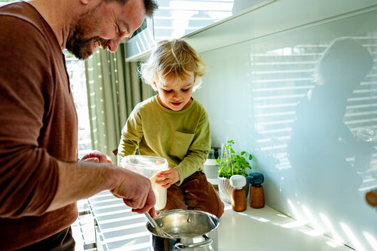 Dad and toddler preparing simple meal together in bright kitchen.