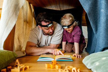 Fototapeta premium Dad and child building and reading book in cozy blanket fort.
