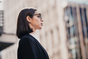 Professional businesswoman in glasses looking confident in city profile portrait near office buildings © deagreez