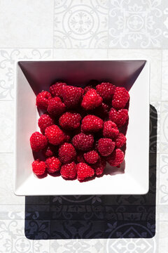 Fresh raspberries in square bowl on patterned tiles