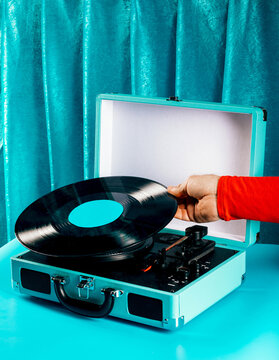 Hand holding retro vinyl record on turquoise suitcase turntable setup