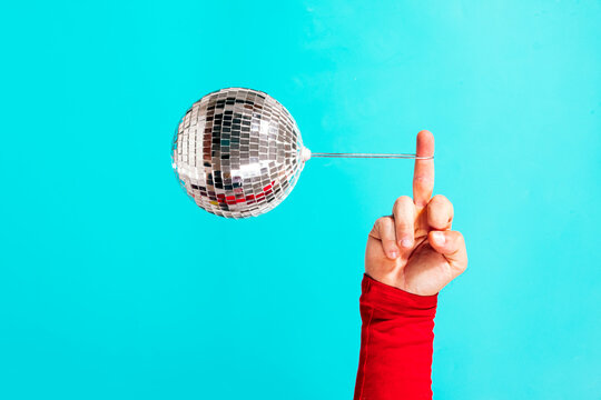 Hand balancing disco ball on finger on blue background