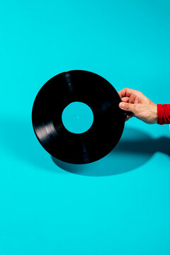 Hand holding vinyl record on turquoise background, retro vibe