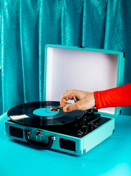 Hand using retro vinyl turntable in turquoise case on blue set