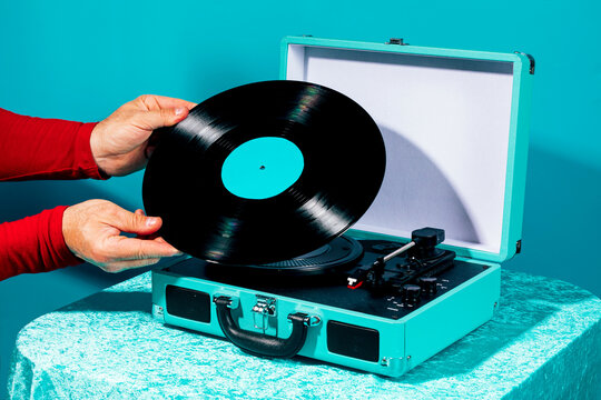 Hands holding retro vinyl record on turquoise suitcase turntable setup