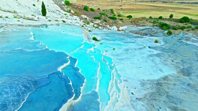 Drone view of Travertines of Pamukkale, Turkey. Turquoise thermal channels, white limestone and green fields create a scenic travel view.