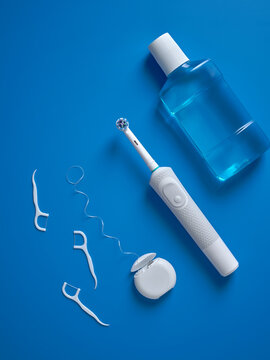 Top view of set a electric toothbrush, dental floss and mouthwash on blue background.