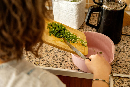 Person adding chopped herb to mixing bowl on kitchen counter