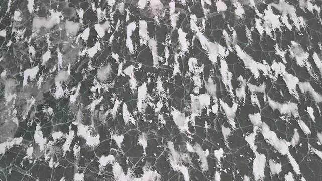 Aerial view of a large frozen lake in winter. The surface is covered by ice, snow, and natural cracks in creating abstract patterns and textures. Cold season landscape. 